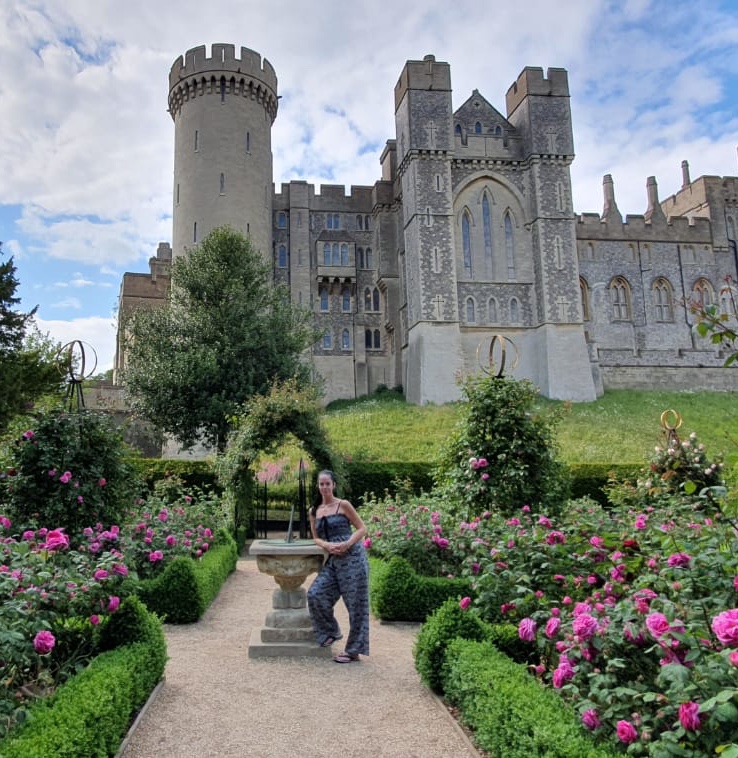 Arundel Castle rose garden woman with dark hair in pony tail posed leaning on a sundial surrounded by big beautiful fascia coloured roses with the castle in full view behind