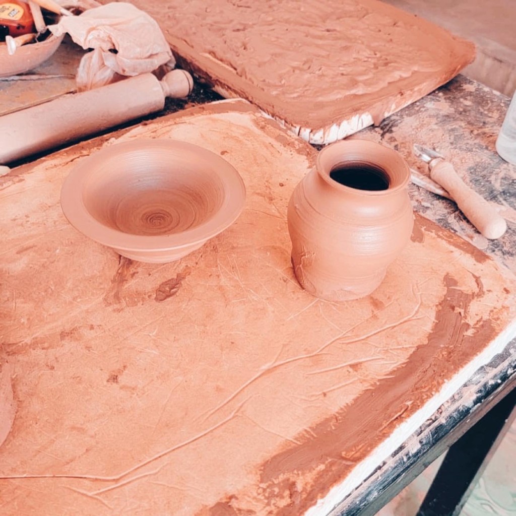 potters table with clay pottery bowl and vase drying on slabs with a rolling pin and other potters tools on the table