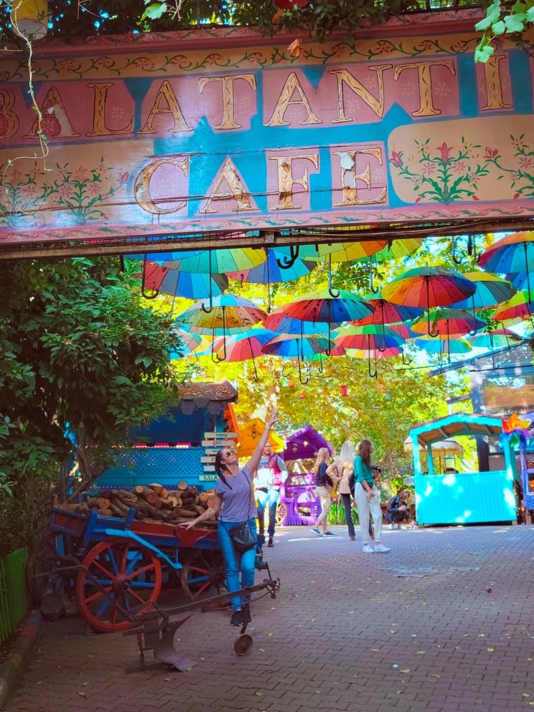 Woman in colourful neighbourhood of Balat reaching up to a covering of umbrellas in an artistic area full of color